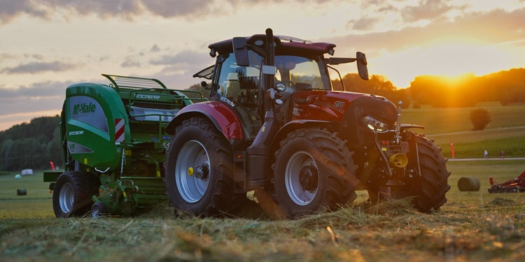 Ein Case IH Maxxum 150 mit einer McHale V6 Ballenpresse im Sonnenuntergang beim ballenpressen im Grünland